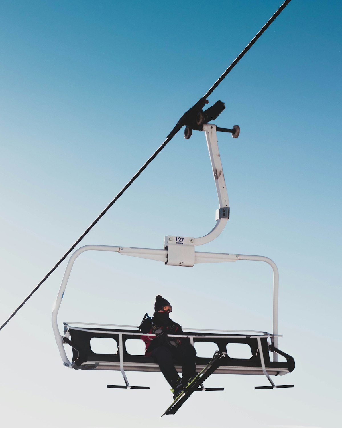 A skier riding a chairlift against a clear blue sky