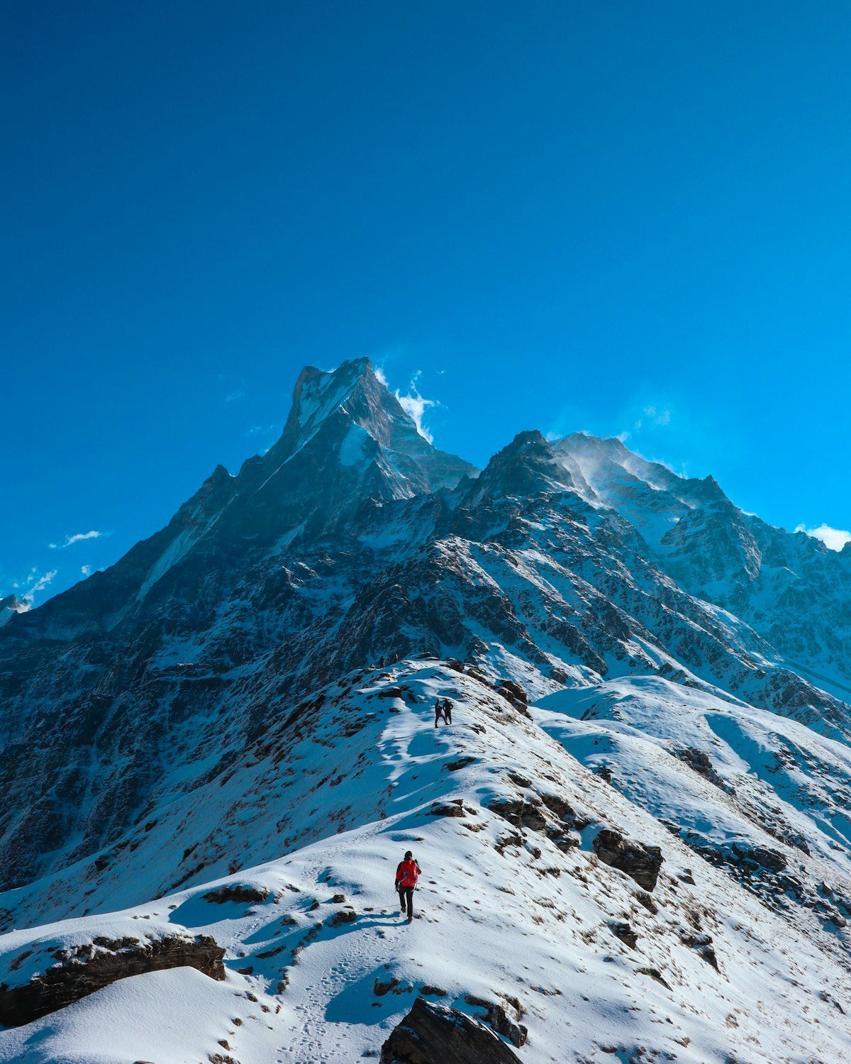 A lone figure walking along a snowy ridge below a high peak