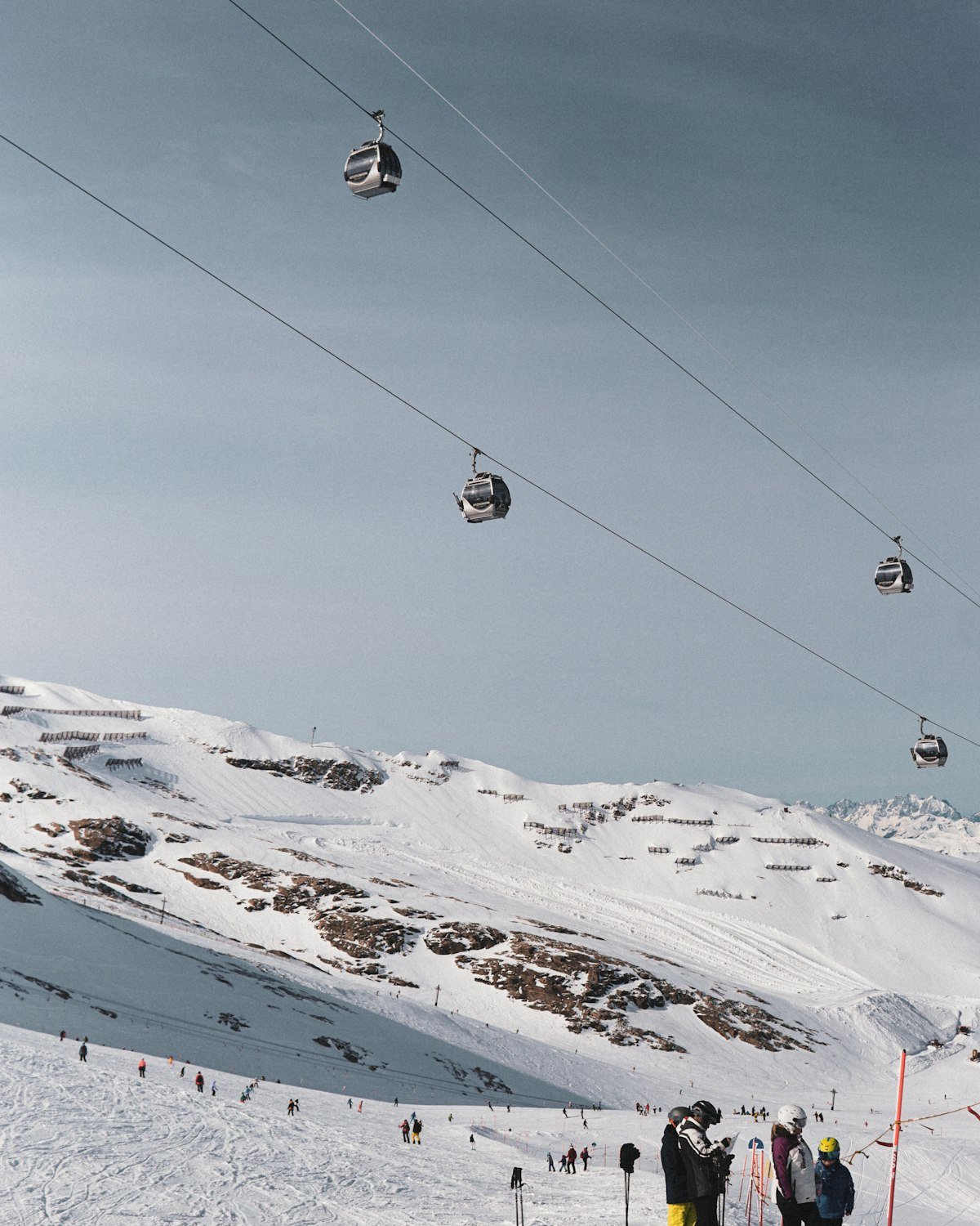 Skiers gathered at the top of a piste beneath a gondola, with snowy slopes beyond